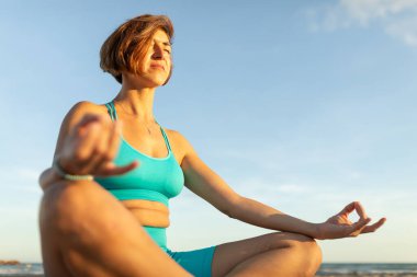 Bir kadın gün batımındaki pilates seansından sonra plajda meditasyon egzersizleri yapıyor.