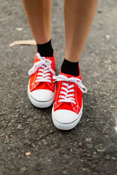 一个年轻女孩的脚 穿着红色的白色橡胶脚尖鞋 站在马路上的沥青路面上 免版税图库图片