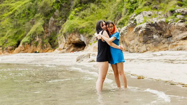 两个年轻姑娘在海滩上散步时 亲切地拥抱在一起 图库图片