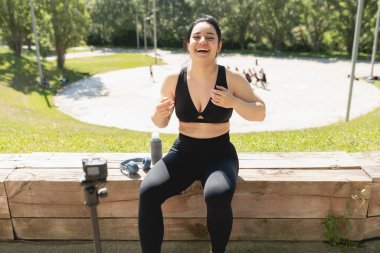 Genç bir kadın, takipçilerine egzersiz ve spor egzersizlerinin nasıl yapıldığını anlatmak için kendini videoya kaydederken mutlu bir şekilde gülüyor.