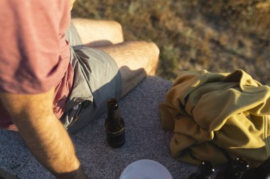 Bira şişesinin yakınındaki genç adam günbatımının tadını çıkarıyor. Galiçya, Kuzey İspanya 'da.