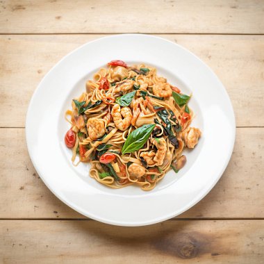 Fried spicy Thai-style seafood spaghetti on a white plate, on a wooden background. selective focus