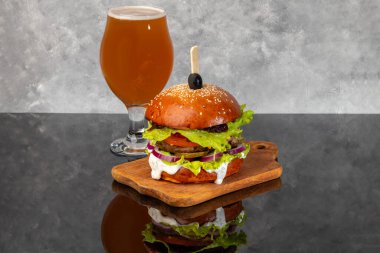 Tahta üzerinde hamburgerle köfte, domates, peynir, salatalık ve marul. Arka planda bir bardak bira. Boşluğu kopyala