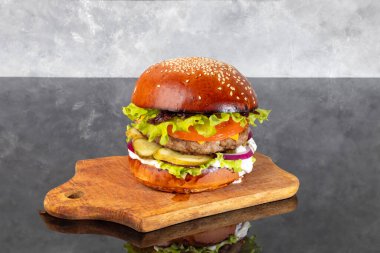 Tahta üzerinde hamburgerle köfte, domates, peynir, salatalık ve marul. Arka planda bir bardak bira. Boşluğu kopyala