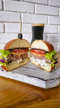 Tahta üzerinde hamburgerle köfte, domates, peynir, salatalık ve marul. Arka planda bir bardak bira. Boşluğu kopyala