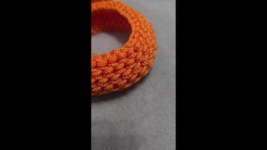 Gri arka planda kordondan örülmüş turuncu bilezik. El yapımı eğilim.