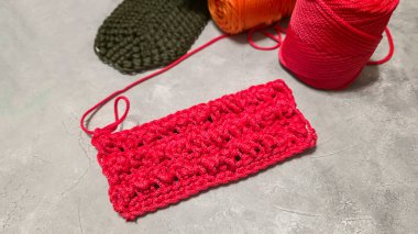 Bir çanta için örgü deseni. Kırmızı polyester kablodan örülmüş. Gri bir arka planda. Desenli tasarım