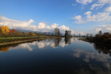 Bulutlu gökyüzü sakin nehire yansıyor