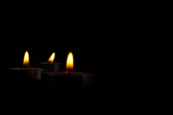 set of three candles lighting and candle with yellow flame in the dark, a Light of candle in the dark, it burns and after a while a gust of wind extinguishes it.