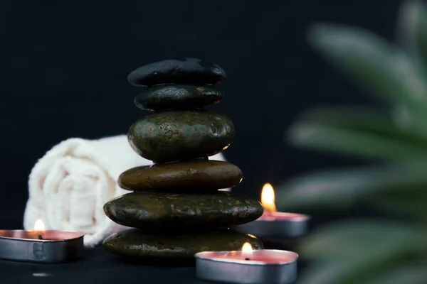 Black hot stones on dark wooden background, layers of hot stones massage setting lit by candles light. Massage therapy for one person with candle light for relax, yoga  concept