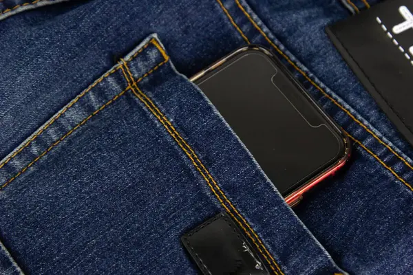 A blue jeans pocket with mobile phone in red