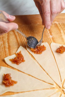 El, Fransız kruvasanı hazırlamak için hamurun üçgenlerine bir kaşık elma reçeli serer. Üst Manzara. Ev yapımı pişirme konsepti