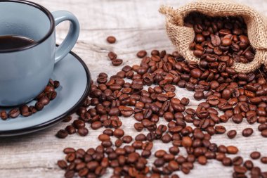 Freshly brewed coffee in a blue cup and coffee beans on a light table. The concept of the morning tradition of drinking coffee.