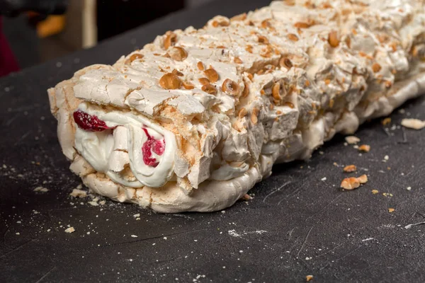Chef confectioner rolls the meringue into a roll with berry confit and cream