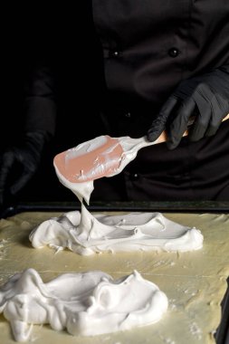 Şekerleme makinesi, fırında daha fazla pişirmek için rulo hamurun üzerine silikon bir spatula ile kremayı yayar.