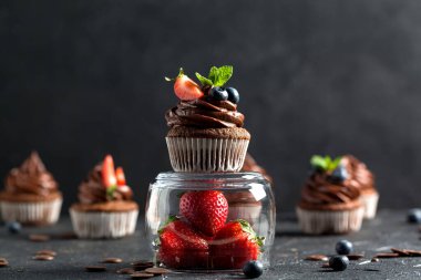 Çikolatalı kekler. Taze yabanmersinli, çilekli ve koyu arkaplanlı taze ev yapımı kekler. Ev yapımı pişirme konsepti. Yumuşak odak