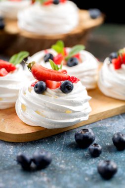 Pavlova tatlısı yapma süreci. Çilek dilimleri, yabanmersini ve nane yapraklı gri arkaplanda Pavlova tatlısı.