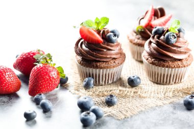 Çikolatalı kekler. Taze yabanmersinli, çilekli ve hafif arkaplanlı taze pişmiş ev yapımı kekler. Ev yapımı pişirme konsepti. Yumuşak odak