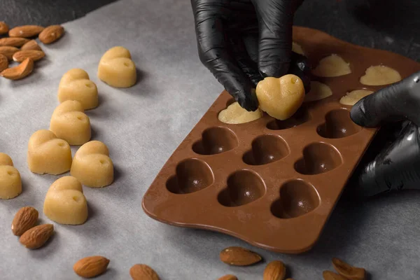 The pastry chef shapes the silicone heart with candy dough in black gloves