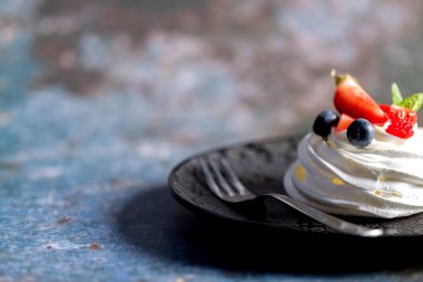 Pavlova tatlısı yapma süreci. Çilek dilimleri, yabanmersini ve nane yapraklı gri arkaplanda Pavlova tatlısı.