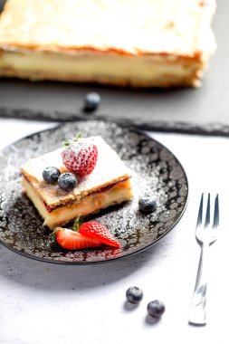Bir parça Napolyon pastası haşhaş tohumu ve kirazla süslenmiş, çilekle süslenmiş, hafif arkaplanlı yaban mersini. Kapat.