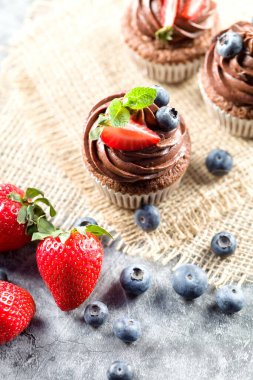 Çikolatalı kekler. Taze yabanmersinli, çilekli ve hafif arkaplanlı taze pişmiş ev yapımı kekler. Ev yapımı pişirme konsepti. Yumuşak odak