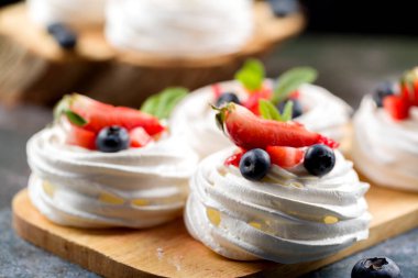 Pavlova tatlısı yapma süreci. Çilek dilimleri, yabanmersini ve nane yapraklı gri arkaplanda Pavlova tatlısı.