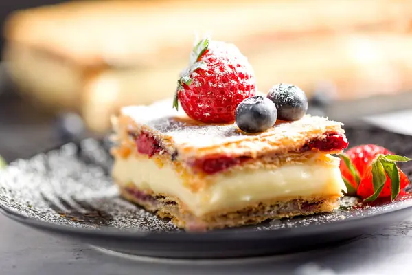 Bir parça Napolyon pastası haşhaş tohumu ve kirazla süslenmiş, çilekle süslenmiş, hafif arkaplanlı yaban mersini. Kapat.