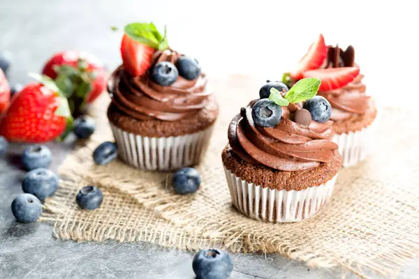 Çikolatalı kekler. Taze yabanmersinli, çilekli ve hafif arkaplanlı taze pişmiş ev yapımı kekler. Ev yapımı pişirme konsepti. Yumuşak odak