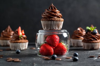 Çikolatalı kekler. Taze yabanmersinli, çilekli ve koyu arkaplanlı taze ev yapımı kekler. Ev yapımı pişirme konsepti. Yumuşak odak