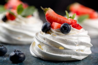Pavlova tatlısı yapma süreci. Çilek dilimleri, yabanmersini ve nane yapraklı gri arkaplanda Pavlova tatlısı.