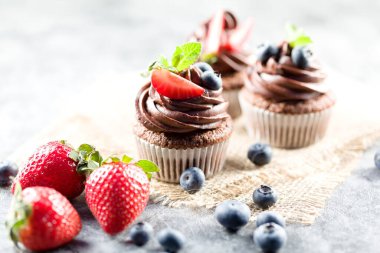 Çikolatalı kekler. Taze yabanmersinli, çilekli ve hafif arkaplanlı taze pişmiş ev yapımı kekler. Ev yapımı pişirme konsepti. Yumuşak odak