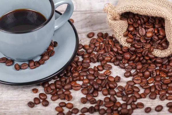 Freshly brewed coffee in a blue cup and coffee beans on a light table. The concept of the morning tradition of drinking coffee.