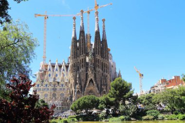 BARCELONA, SPAIN - 12 Mayıs 2017: Bu, Gaudi Meydanı 'nda göleti olan bir parktan 100 yıldan fazladır inşaat halinde olan Sagrada Familia Bazilikası' nın bir görüntüsü..