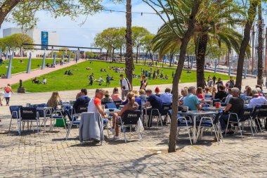 BARCELONA, SPAIN - MAY 10, 2017: Unidentified people relax in a cafe and on the lawn of the park near the marina of the Old Port.