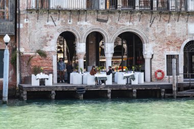 VENICE, İTALYA - 12 MARTH 2023: tanımlanamayan müşteriler eski bir evdeki bir kafede kahvaltı yapıyorlar ve bahar sabahının erken saatlerinde Büyük Kanal 'da bir iskelesi var..