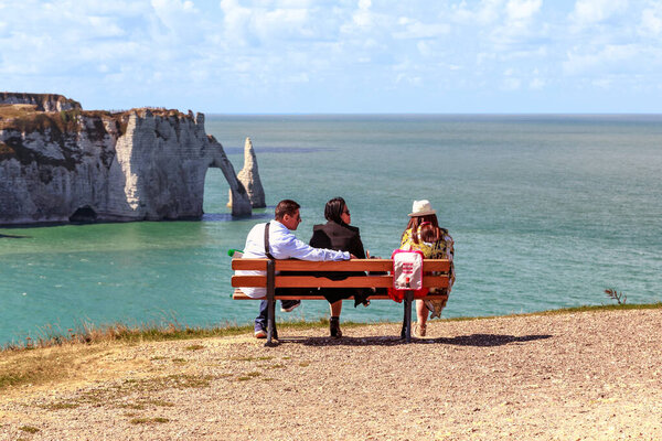 ETRETAT, FRANCE - SEPTEMBER 1, 2019: This is a group of unidentified vacationers on a bench on the edge of a cliff overlooking the coastline of the Alabaster Coast.