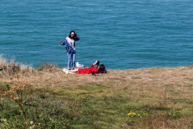 ETRETAT, FRANCE - 1 Eylül 2019: 2 kimliği belirsiz genç kadın okyanusa bakan bir uçurumun kenarında dinleniyor..