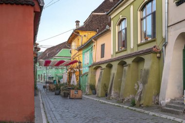SIGHISOARA, ROMANIA - 2 Mayıs 2023: Bu eski kasabada boş bir kafe ve sabah erken saatlerde kale duvarları olan eski bir yaya sokağı.
