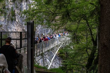 SCHWANGAU, ALMANY - 23 Mayıs 2024 'te Pellat Vadisi üzerindeki Maria Köprüsü' nde nefes kesici manzaralar sunan kimliği belirsiz turist kalabalığı..