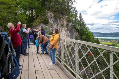 SCHWANGAU, GERMANY - 23 Mayıs 2024: Tanımlanamayan turistler, nefes kesici manzaralar sunan Pellat Vadisi üzerindeki Maria Köprüsü 'nde fotoğraf çekiyorlar.