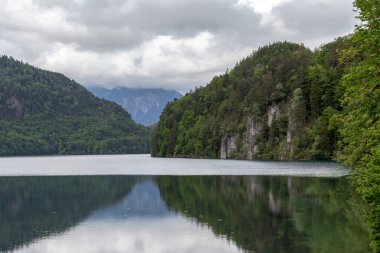 SCHWANGAU, ALMANY - 23 Mayıs 2024 Bu Alpsee dağının bulutlu bir bahar günü manzarası.