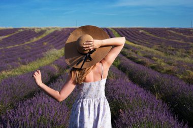 Şapkalı genç bir kadın lavanta tarlasının arka planında duruyor. Modelin arkasındaki portre. Gün ışığı