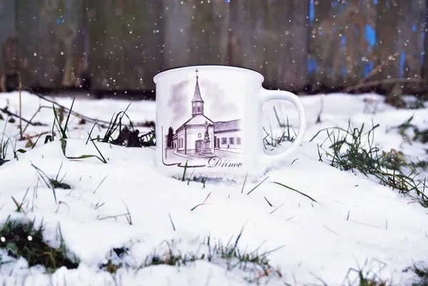 a coffee cup sitting in the snow in front of a fence