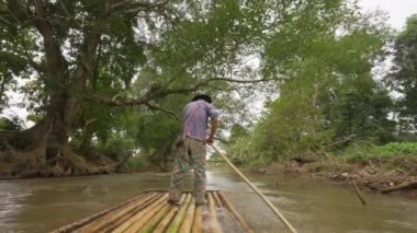 Chiang Mai, Thailand - 5 December 2022 - Back of a local man on bamboo raft using a long bamboo pole to push his raft down a small river in Chiang Dao, Chiang Mai, Thailand