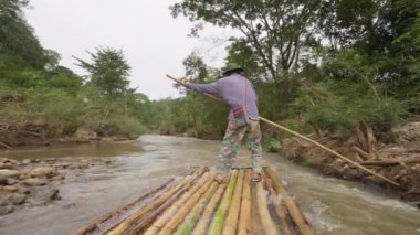 Chiang Mai, Thailand - 5 December 2022 - Back of a local man on bamboo raft using a long bamboo pole to push his raft down a small river in Chiang Dao, Chiang Mai, Thailand