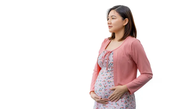 身穿母性服装的快乐年轻而务实的亚洲女人笑着站在一个白色的背景前 一边抱着肚子一边想着她的孩子 一边在左边留有复制的空间 — 图库照片