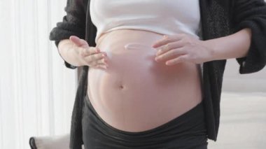 Salata kasesinden sağlıklı kırmızı vişneli domatesini yiyen günlük hamile Asyalı kadın oturma odasının penceresinin önünde duruyor.