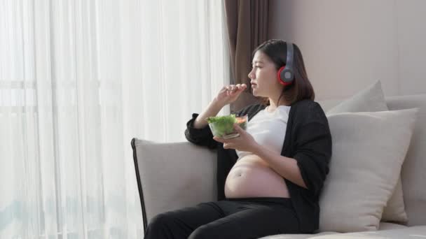 Счастливая Азиатская Беременная Женщина Ест Свой Здоровый Салат Слушая Музыку — стоковое видео