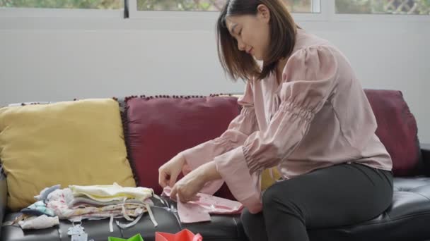 Νεαρή Έγκυος Ασιάτισσα Που Βλέπει Χαρούμενα Καινούργια Της Μωρουδιακά Ρούχα — Αρχείο Βίντεο